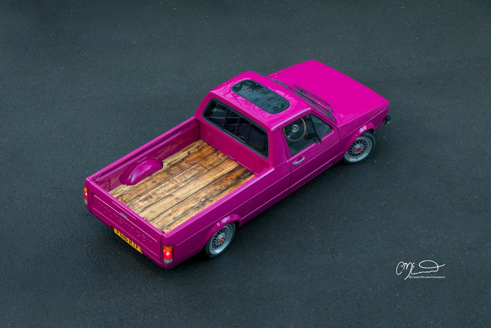 vintage Volkswagen Caddy pickup truck A vintage pink pickup truck with a wooden bed on a dark asphalt surface, photographed from above.