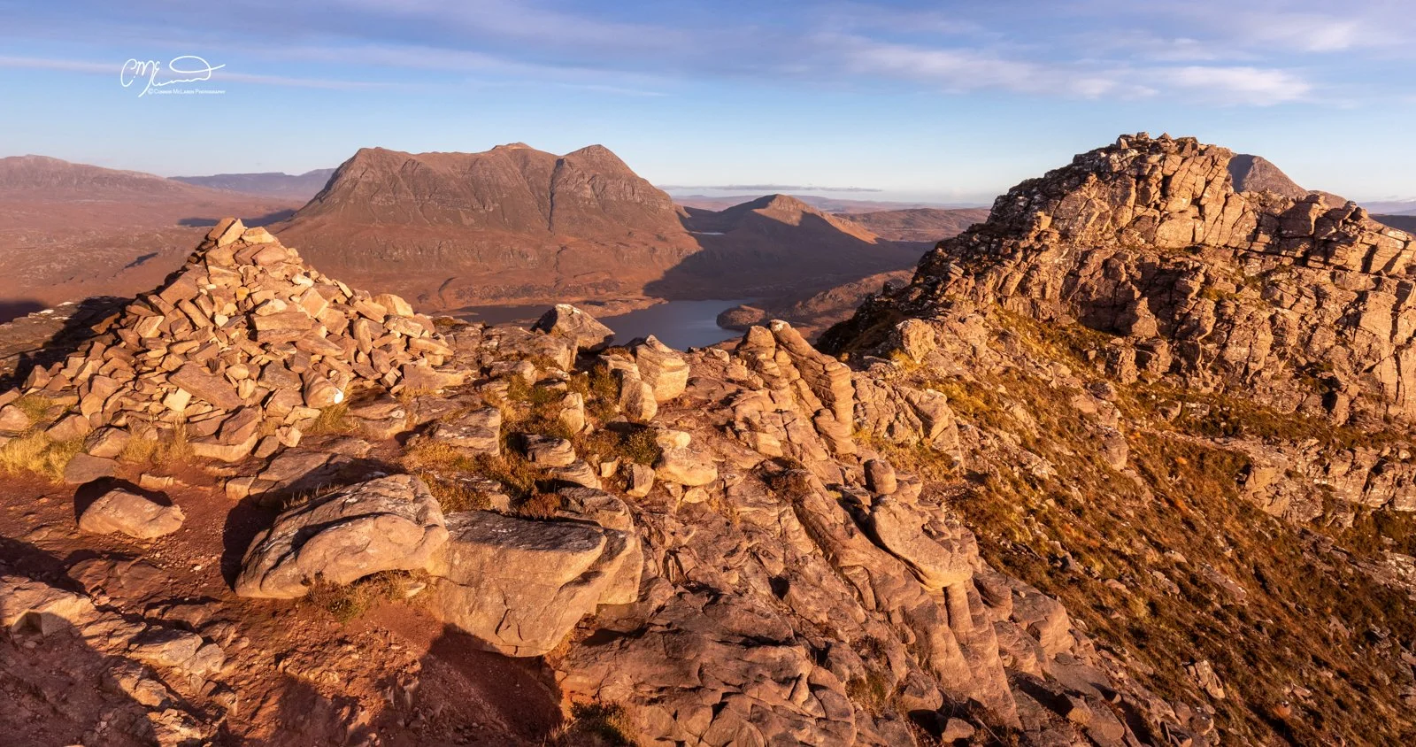 Scotland, north coast 500, NC500, Assynt. Stac Pollaidh. Rocks and boulders on a mountain trail overlooking a lake, with mountains in the background during sunset.