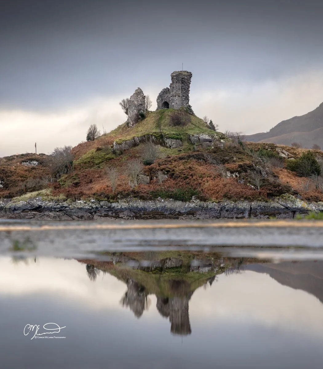 Scotland, Isle of Skye, caisteal Maol. Ruined stone castle on a hill reflected in a body of water with dark cloudy sky.