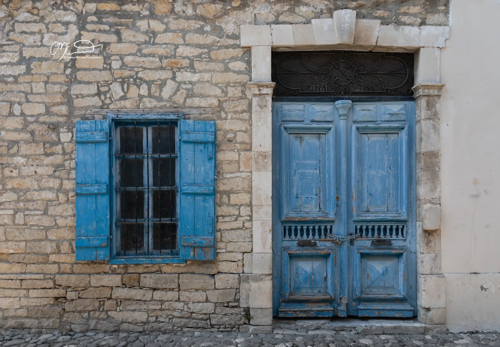 Limassol, Cyprus. Blue wooden window with shutters and a blue double door with a chain lock, set in a stone wall.
