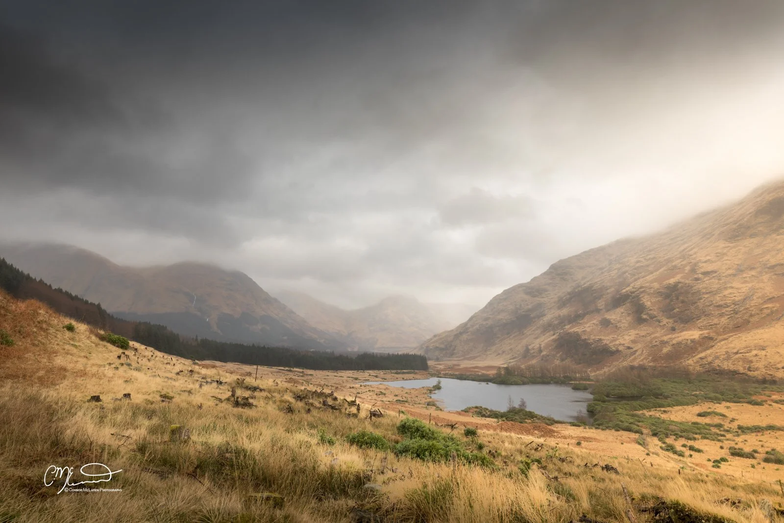 Glen Coe and Glen Etive, Western Highlands, Scotland. A scenic landscape with mountains, a cloudy sky, a lake, and grassy fields in a valley.