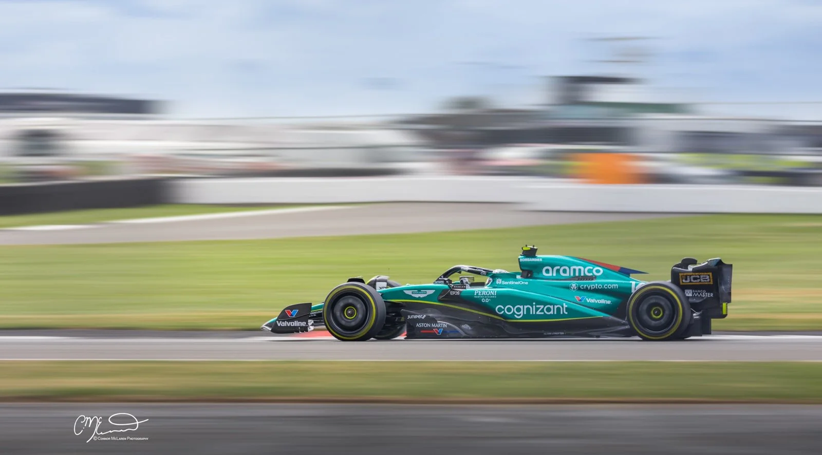 Alonso, Aston martin teal Formula 1 race car driving on a race track with motion blur in the background.