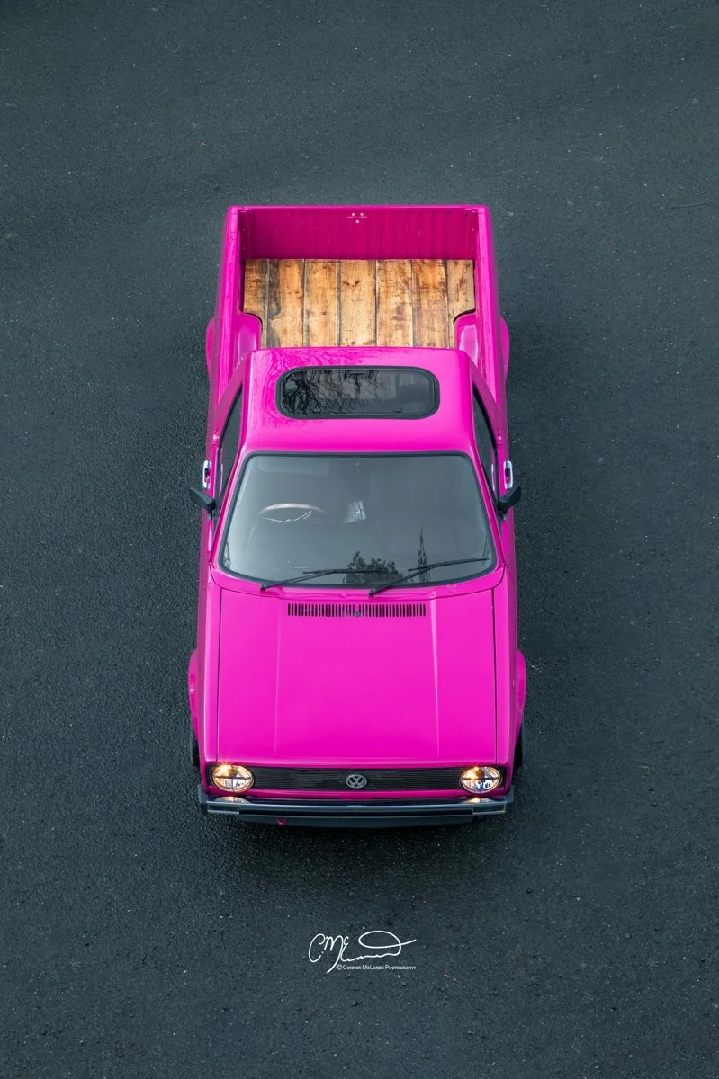 vintage Volkswagen Caddy pickup truck A top-down view of a bright pink pickup truck with a wooden cargo bed parked on a dark asphalt surface.