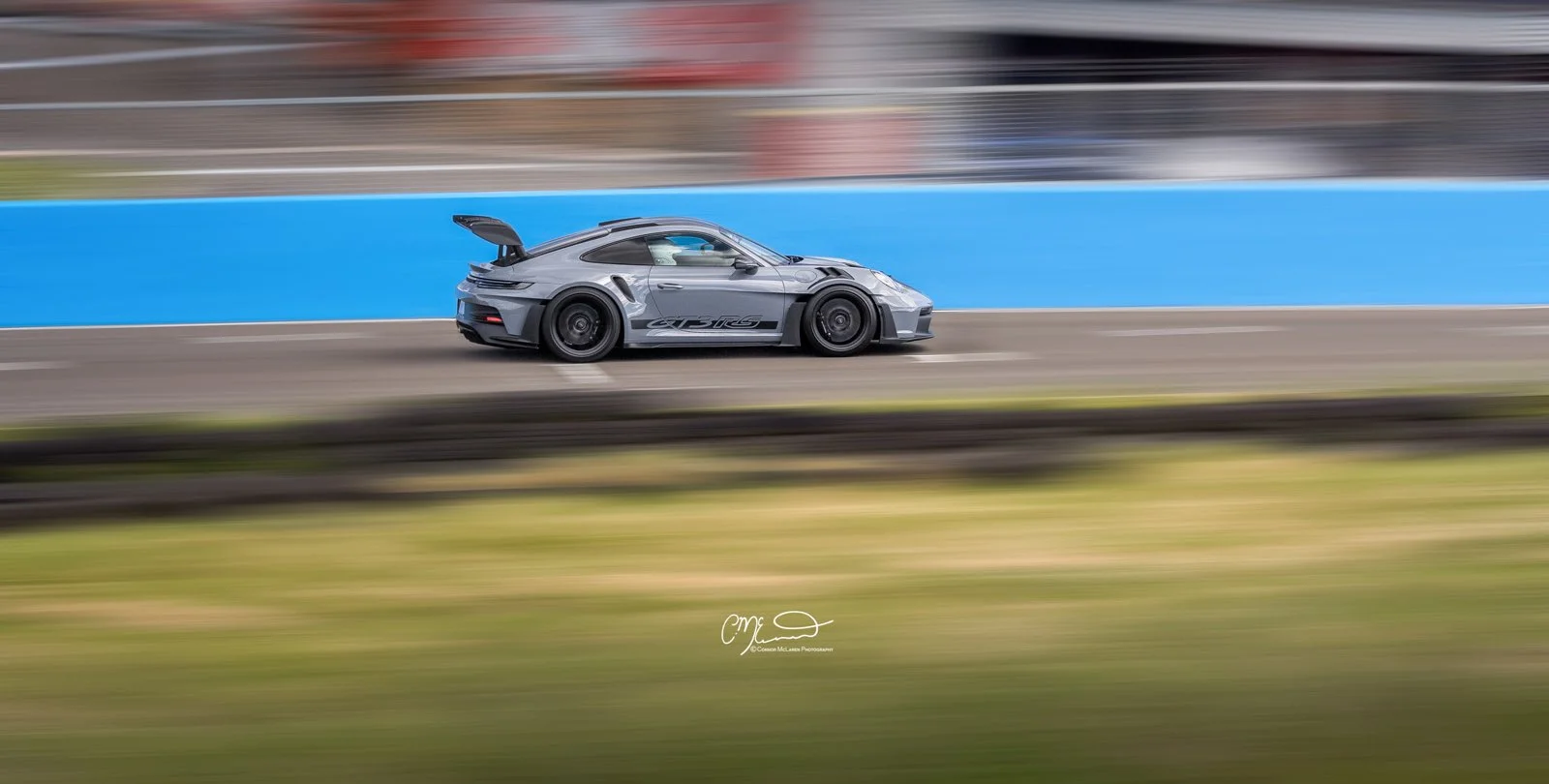 Porsche 911 GT3 RS, 992 racing at knockhill. A sleek gray sports car racing on a track with motion blur indicating high speed, with blurred background and foreground.