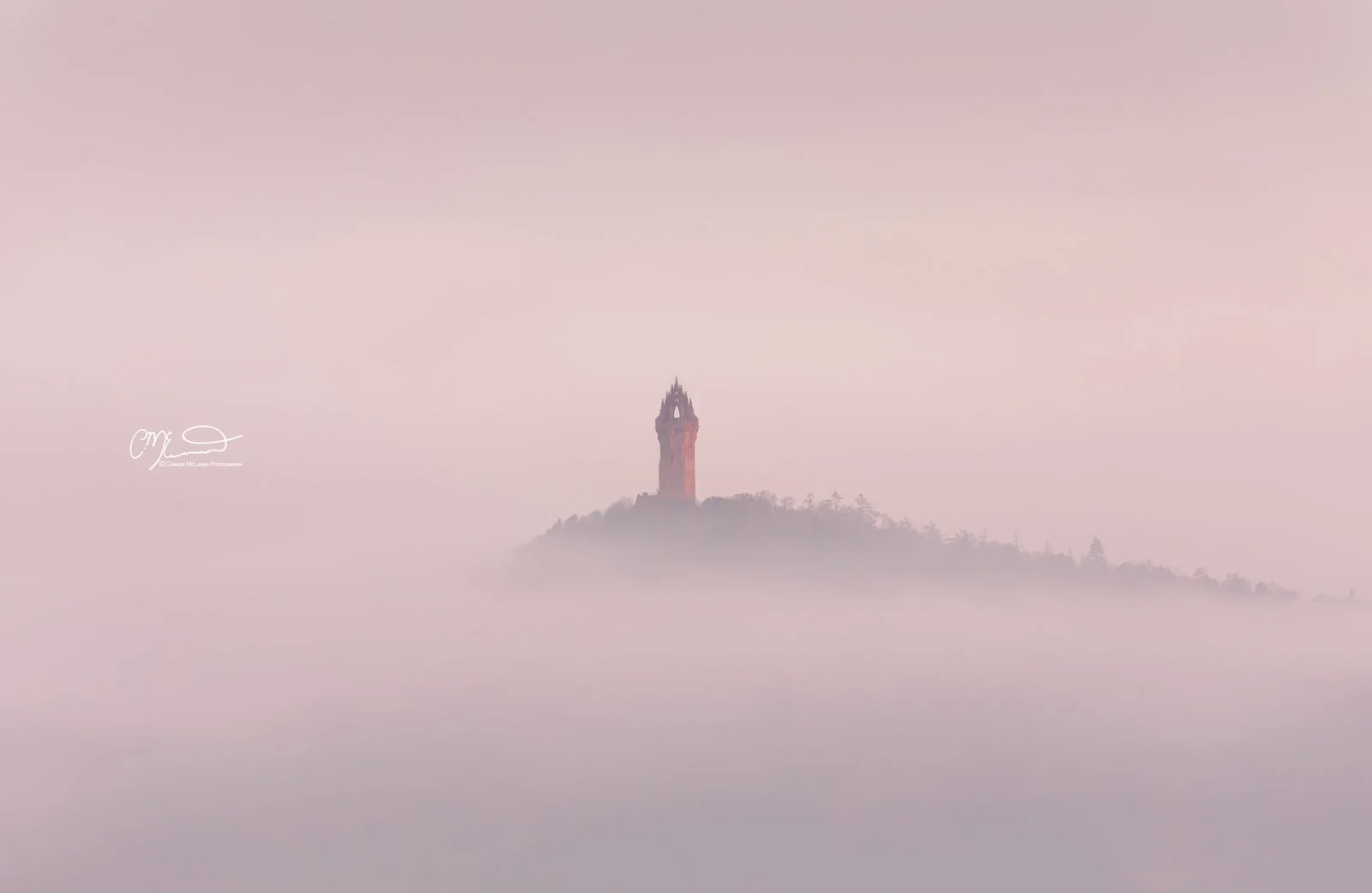 Scottish Lowlands, Scotland, william wallace monument stirling. A tall, ornate tower on a hilltop surrounded by mist and fog, with a pink and purple sky in the background.