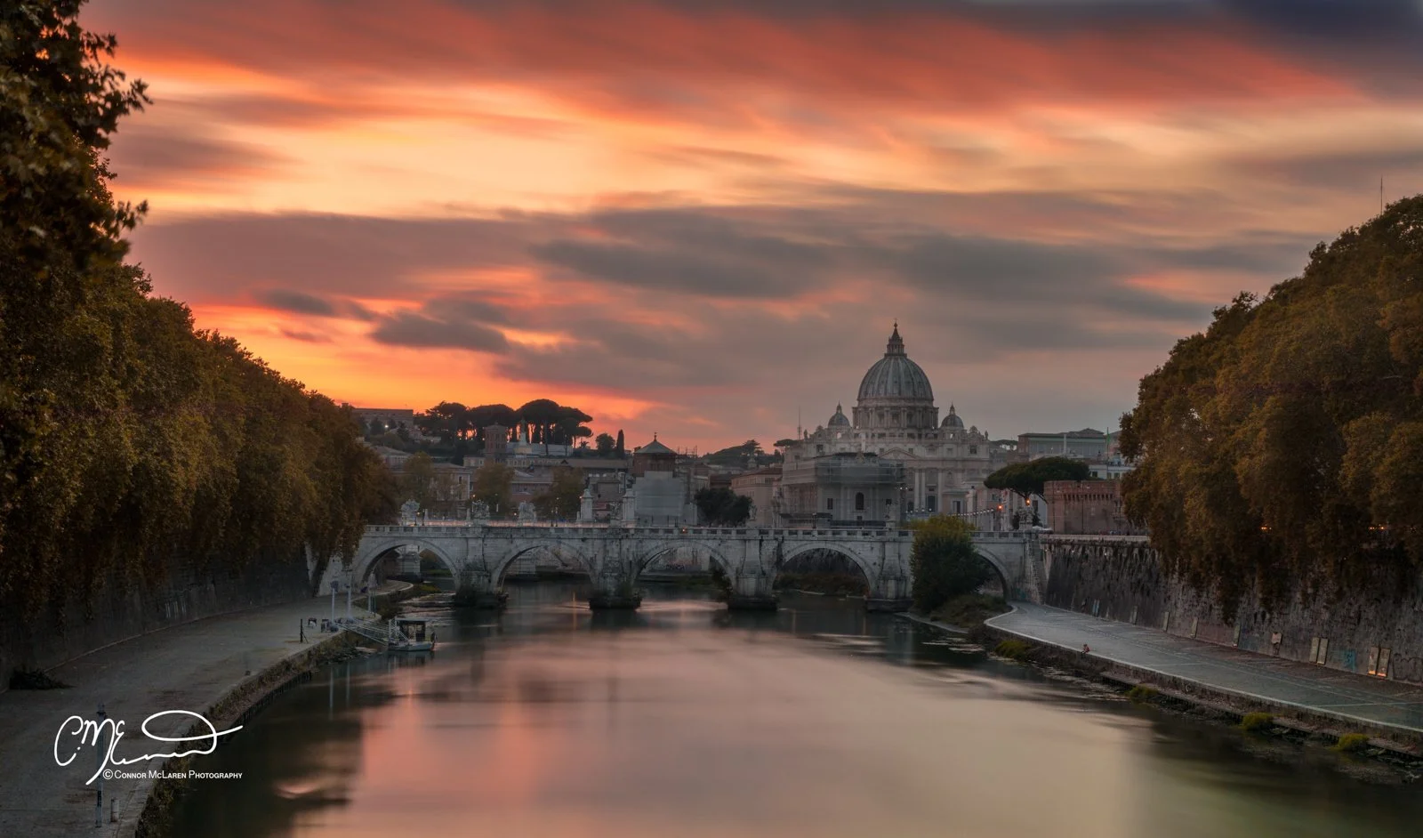 Roman Forum and colosseum, Rome & the vatican. A scenic view of the Roman Catholic St. Peter's Basilica in Vatican City at sunset, with a river and bridge in the foreground, surrounded by trees and cityscape.