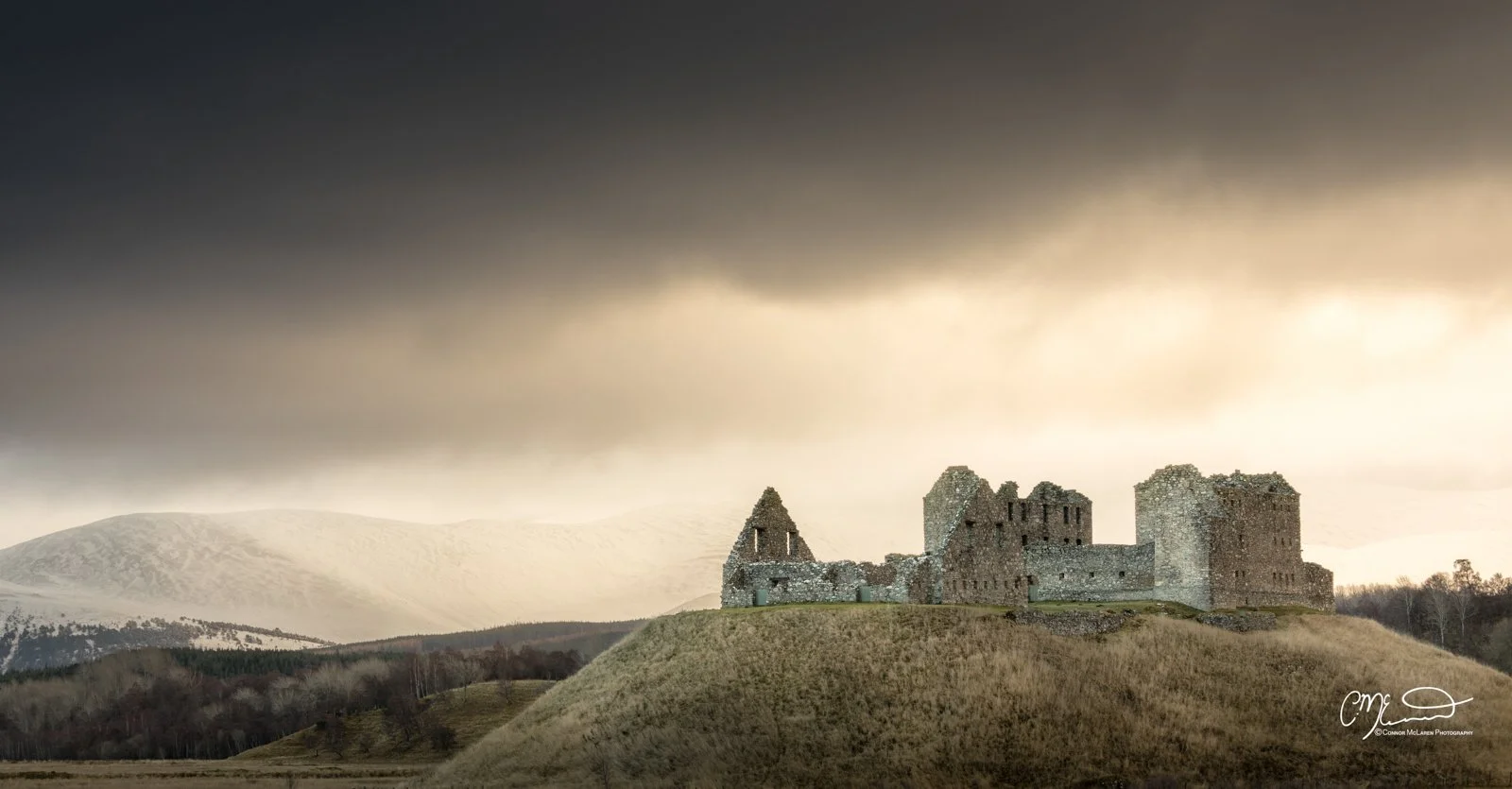 Scottish Central Highlands, Scotland, cairngorms ruthven barracks. Ruins of an old stone castle on a grassy hill with mountains in the background and a dark cloudy sky overhead.