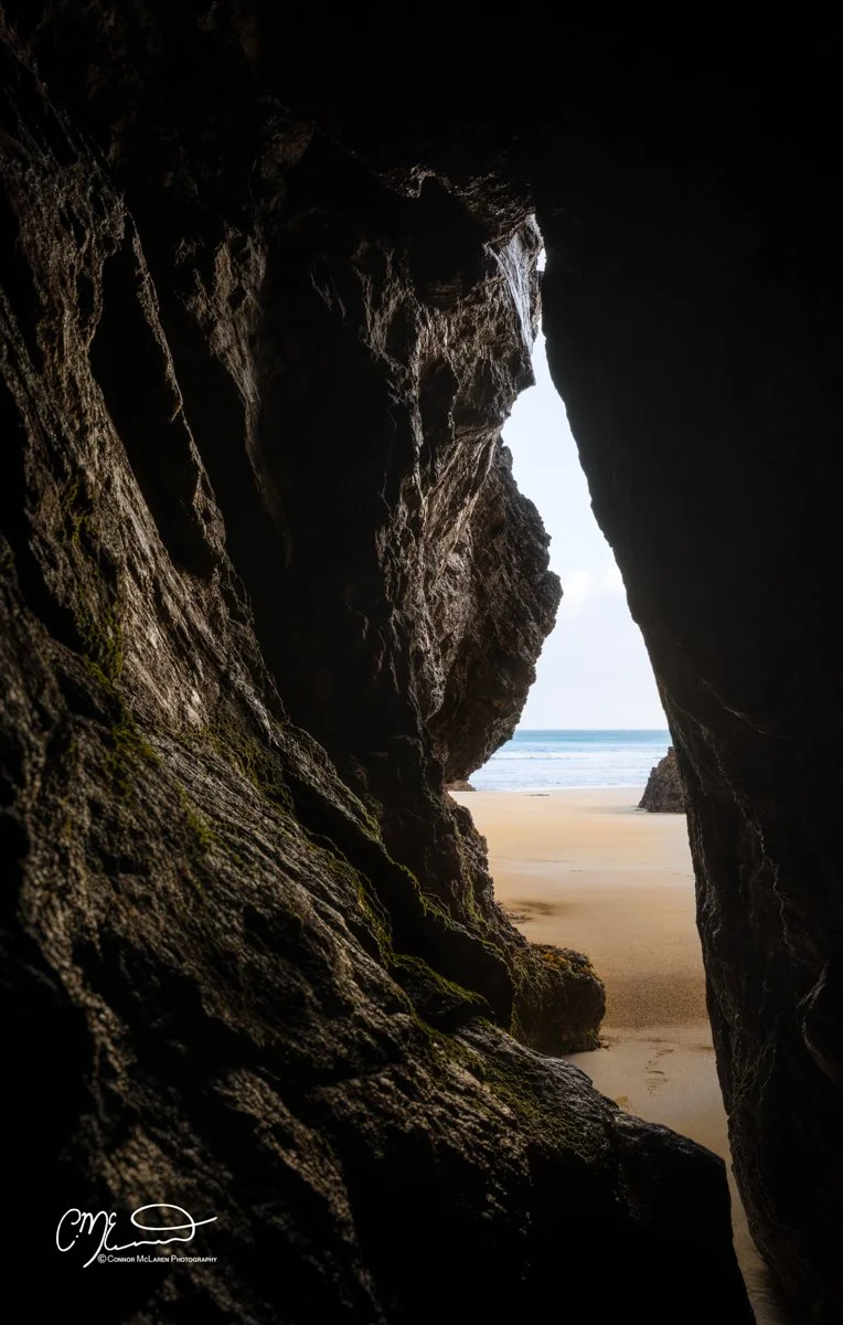 Scotland, Lewis Harris & Outer Hebrides, Tolsta. View from inside a rocky cave looking out onto a sandy beach and ocean waves.