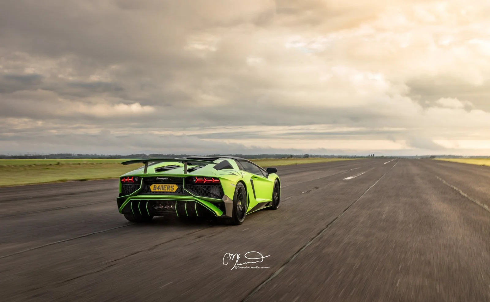 Lamborghini Aventador SV roaster on runway. A lime green Lamborghini sports car driving on an empty runway or road under a cloudy sky.