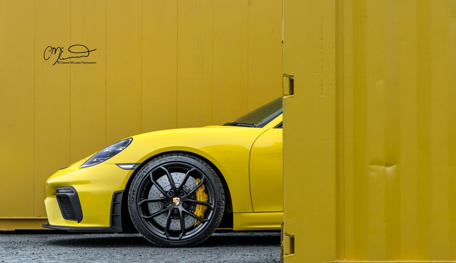 Partial view of a yellow Porsche Spyder  sports car behind a yellow container.