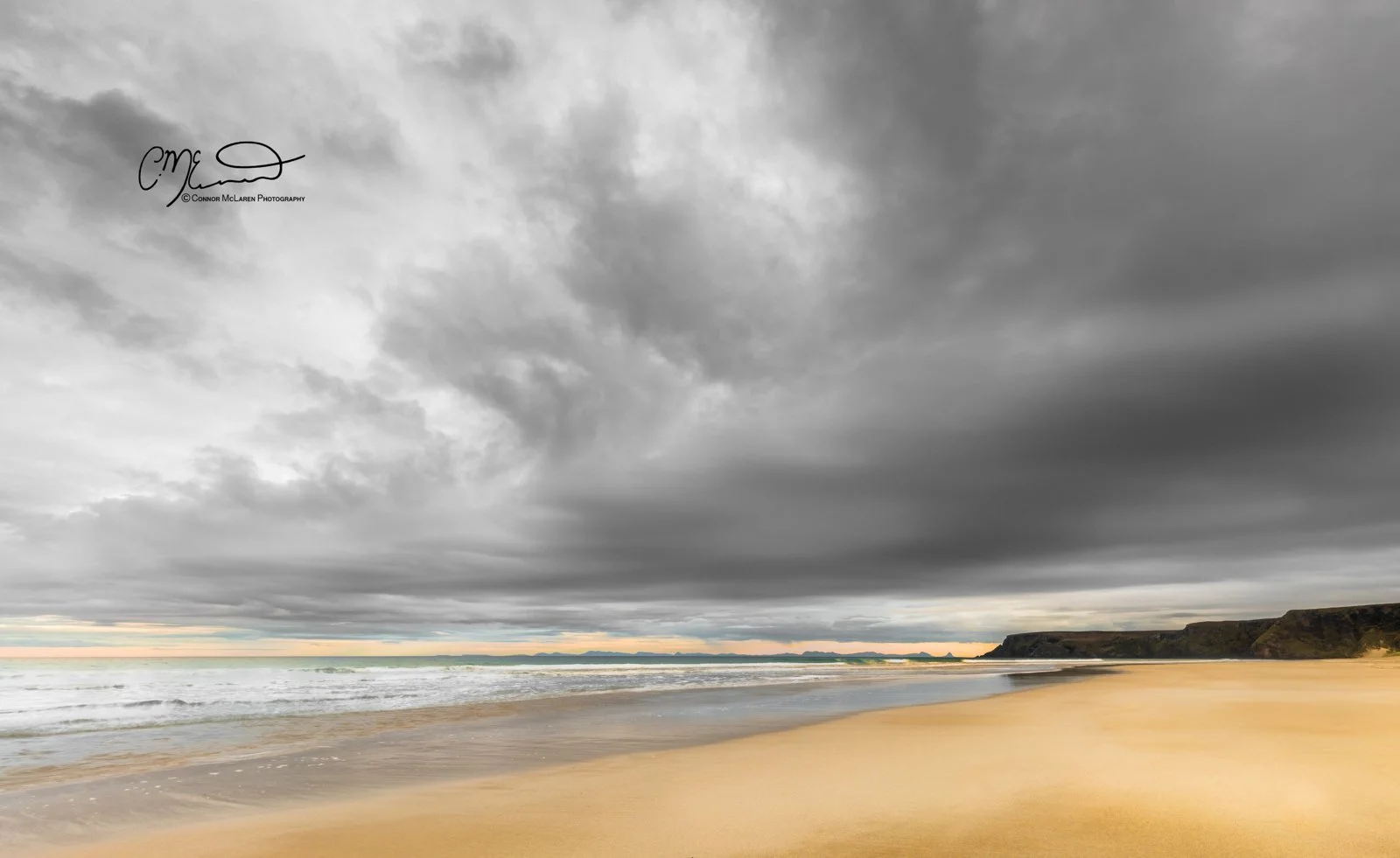 Scotland, Lewis Harris & Outer Hebrides, Tolsta. A beach with golden sand, ocean waves, and a cloudy sky overhead, with cliffs in the distance.