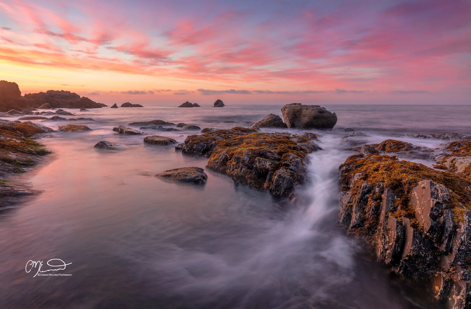 Morrayshire, North East Scotland. Sunset over rocky shoreline with moss-covered rocks and calm ocean waves.