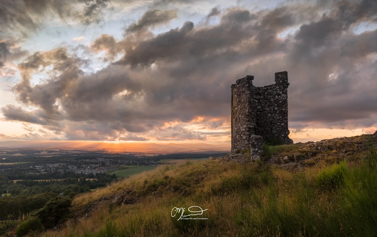 Scottish Central Highlands, Scotland, Perthshire Scone. A stone castle tower on a hill during sunset with a cloudy sky and a distant town in the background.