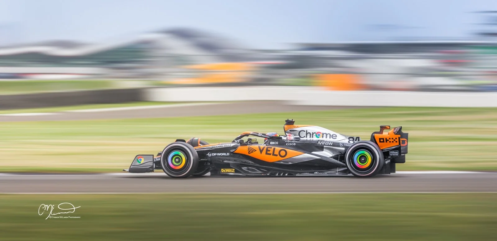 Formula One, Oscar Piastri, McLaren F1 car racing at Silverstone in limited edition livery for one race only. A race car moving at high speed on a racetrack with a blurred background, featuring sponsors like Chrome, Velo, and OKD.