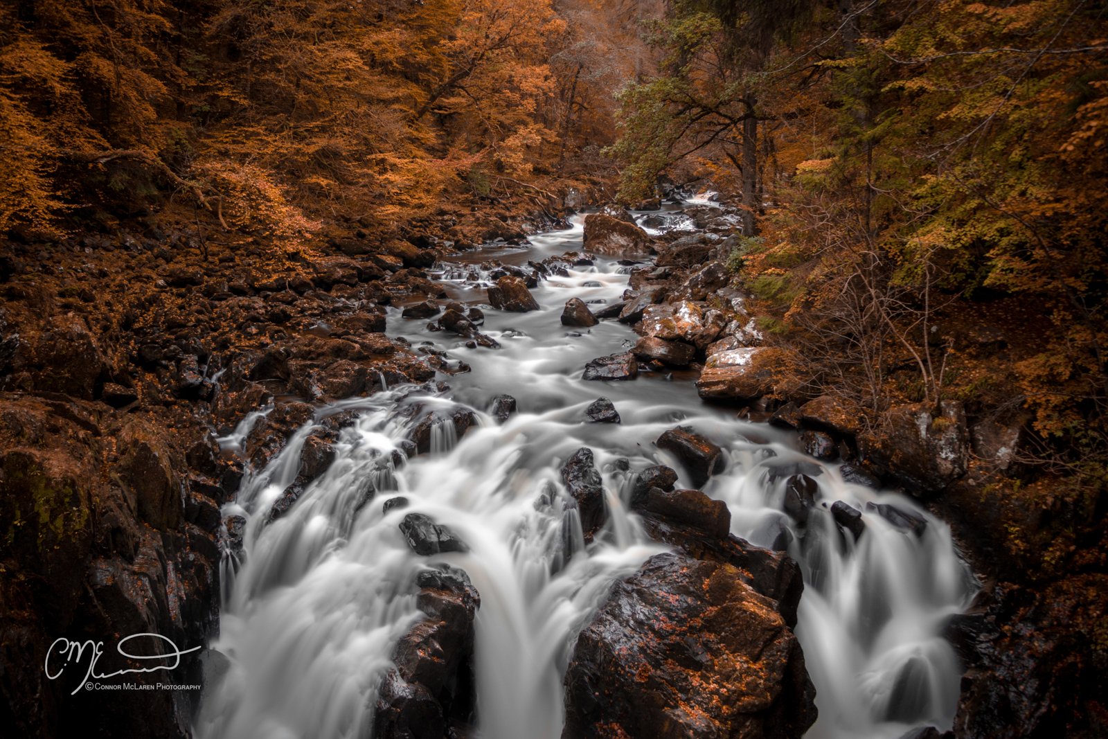 Scottish Central Highlands, Scotland, Perthshire Hermitage. A waterfall flowing over rocks in a forest with autumn foliage.
