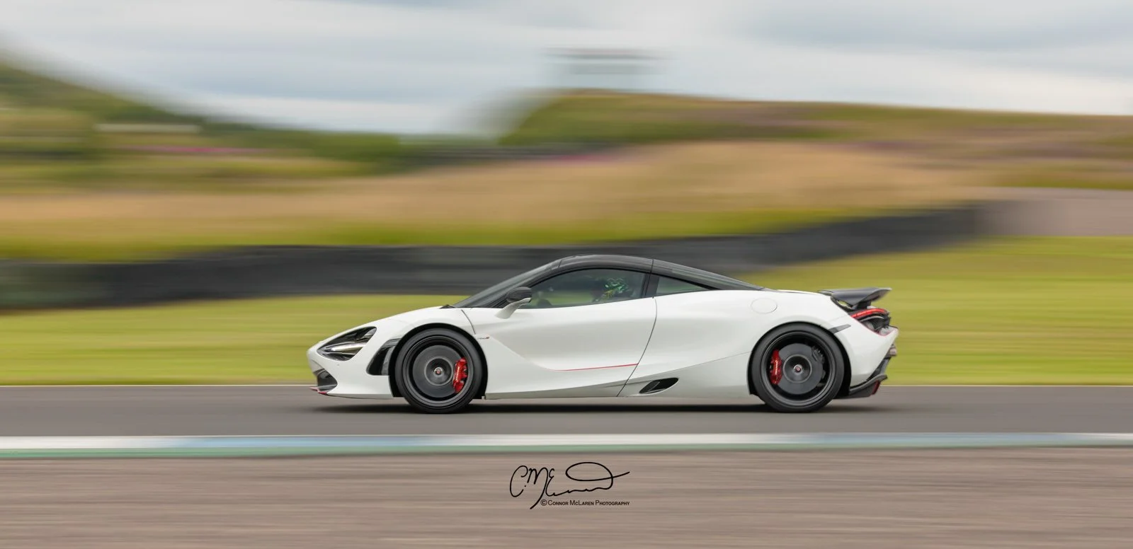McLaren 720S racing on track at Knockhill. A white sports car with black roof and red brake calipers racing on a track, blurred background indicating high speed.