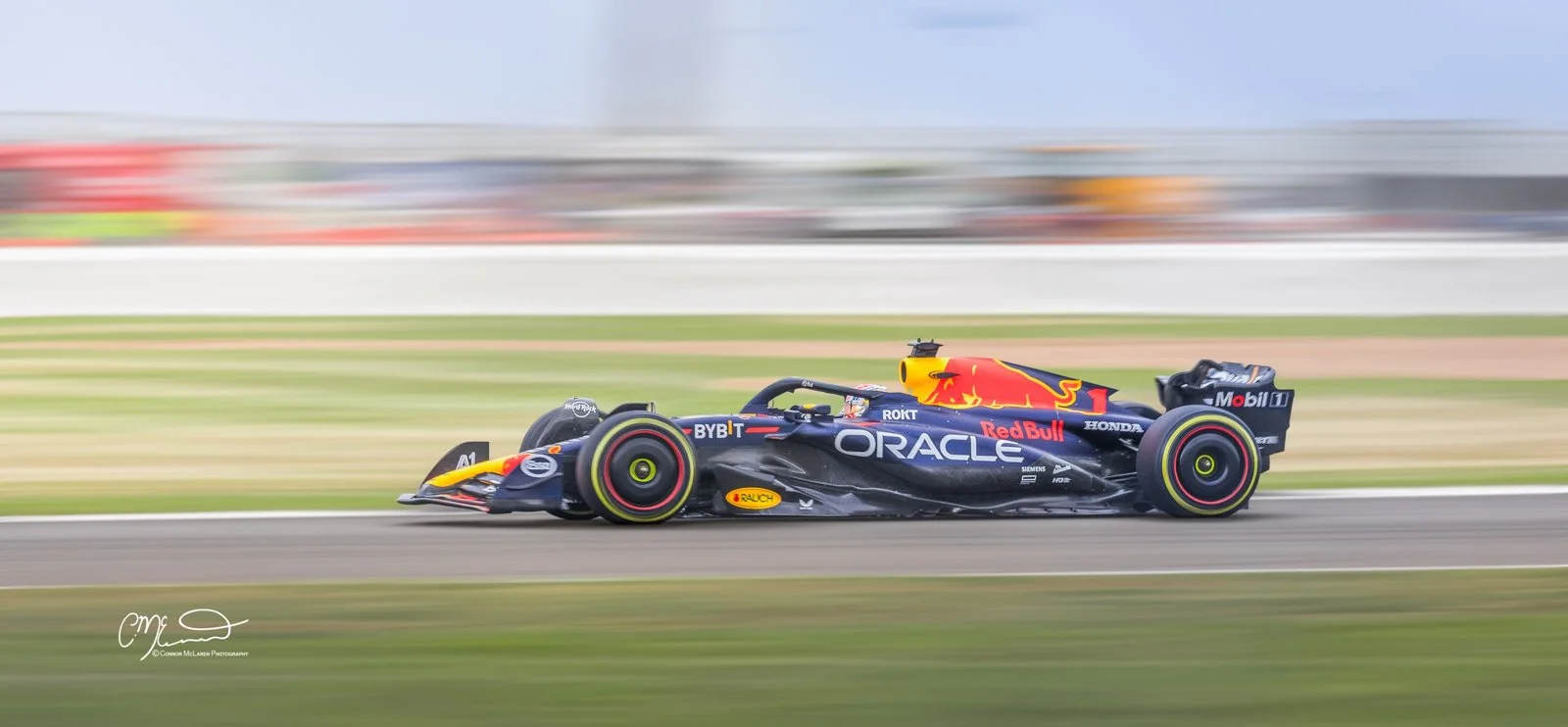 Red Bull formula one car being driven by world champion max verstappen at silverstone. Formula 1 race car on a race track, with sponsor logos including Red Bull, Oracle, and Honda, in motion blur background.