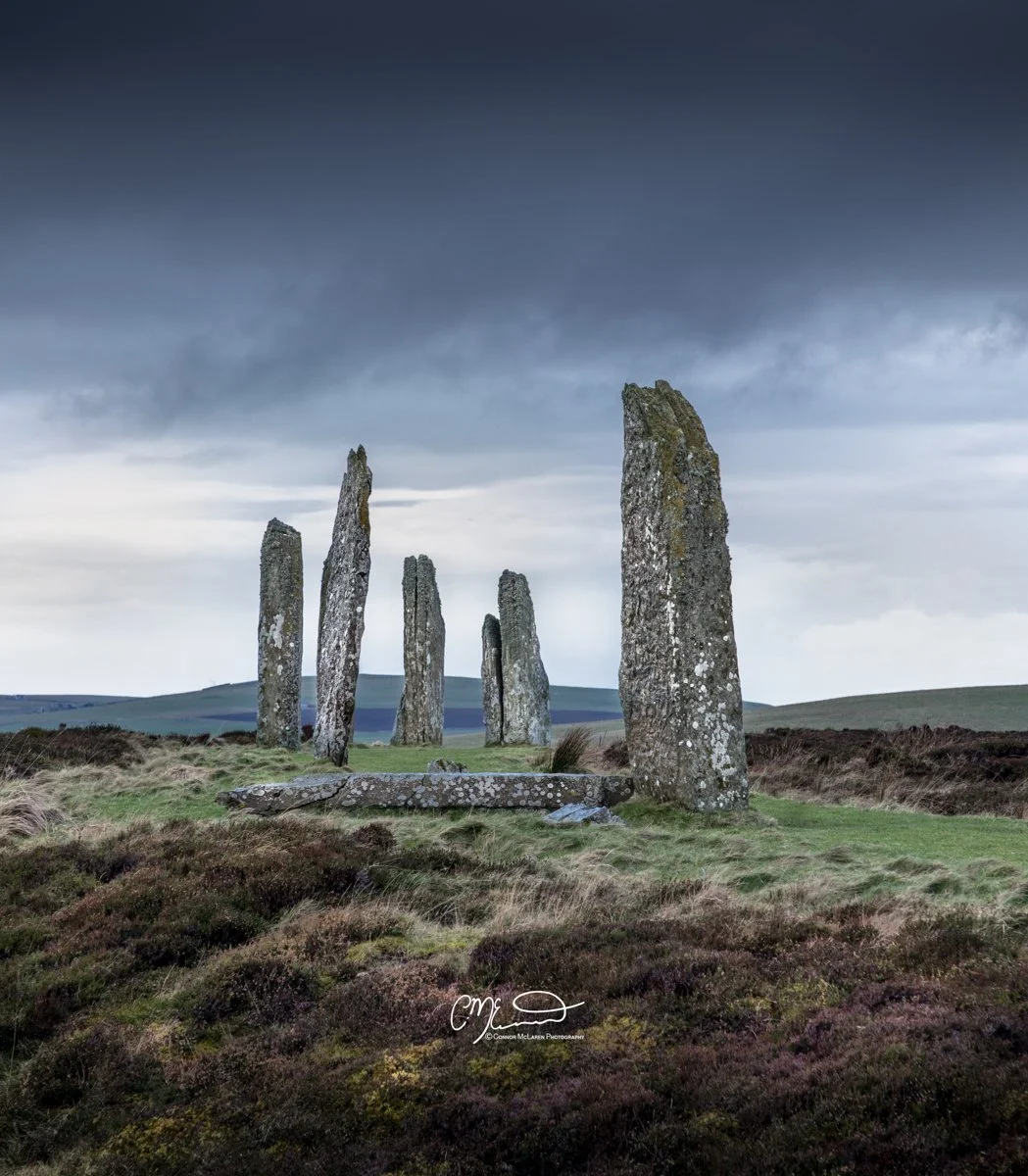 Ring of Brodgar, Orkney, Scotland. Scenic view of ancient standing stones arranged in a line on a grassy landscape under a dark, cloudy sky.