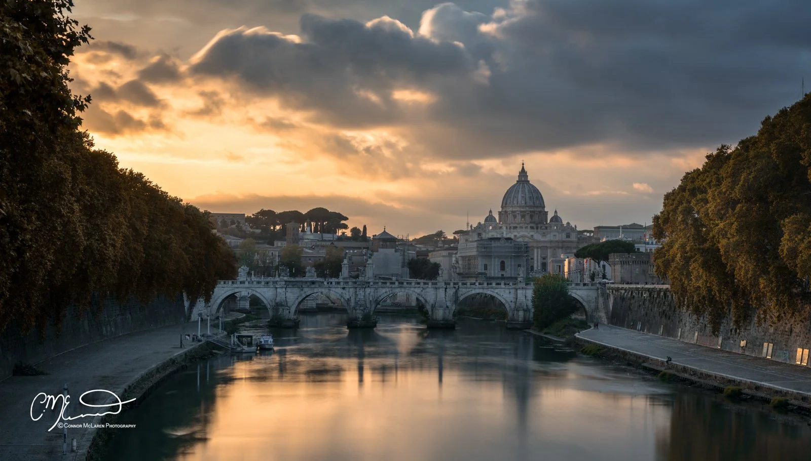 Roman Forum and colosseum, Rome & the vatican. A scenic view of the Tiber River in Rome at sunset, featuring a historic bridge and the dome of St. Peter's Basilica in the background under a partly cloudy sky.