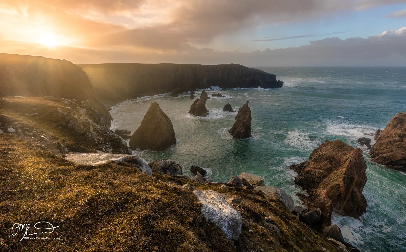 Scotland, Lewis Harris & Outer Hebrides, Mangersta. Sunset over coastal cliffs with large rocks in the ocean and grassy foreground