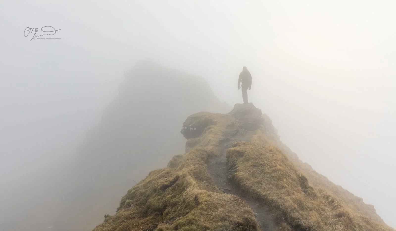 Scottish Central Highlands, Scotland, Perthshire munro. A person standing on a narrow, rocky mountain trail surrounded by thick fog.