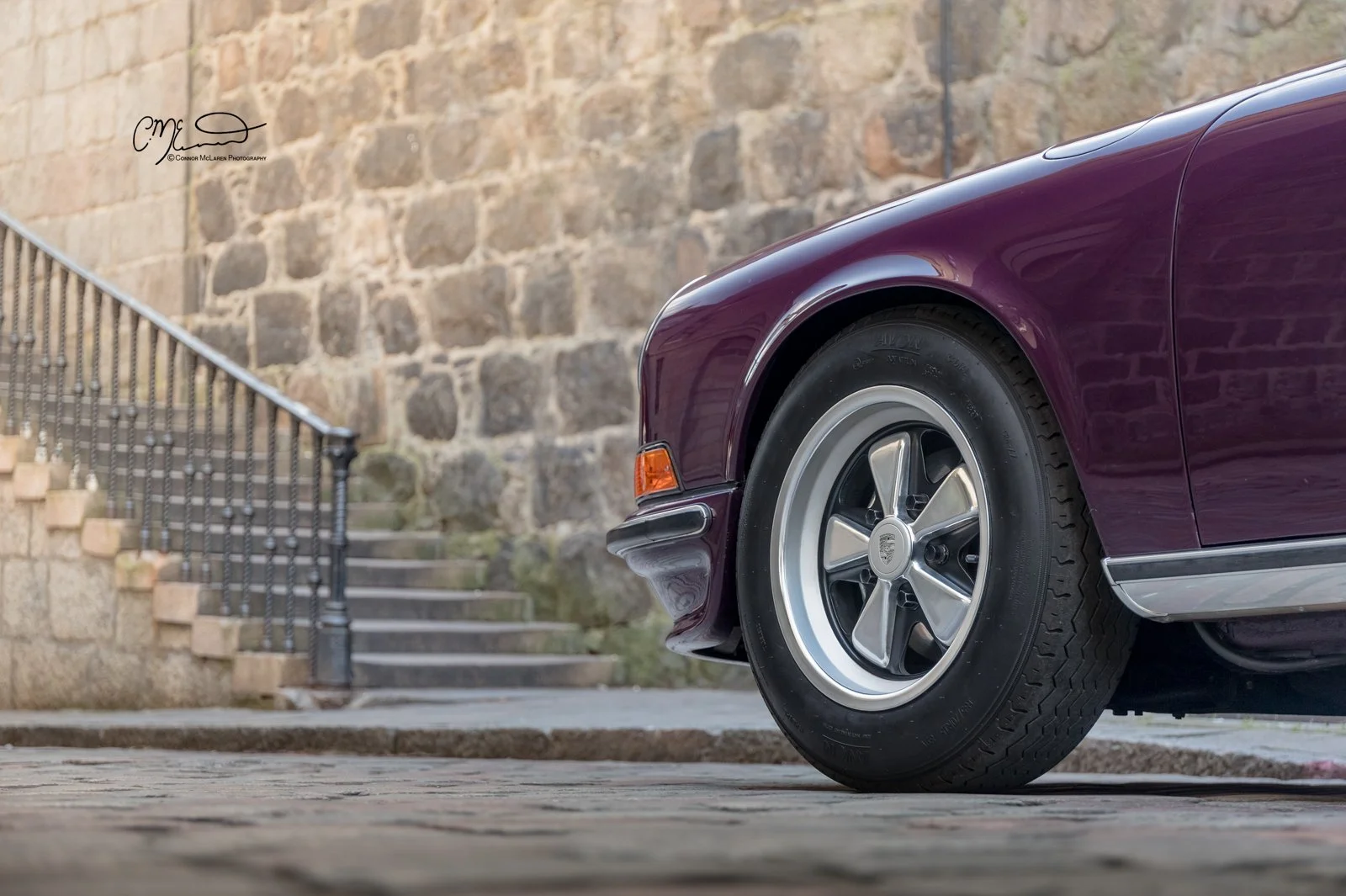 Porsche 911, 2.7RS. Close-up of a vintage purple Porsche car parked on a cobblestone street with a stone wall and stairs in the background