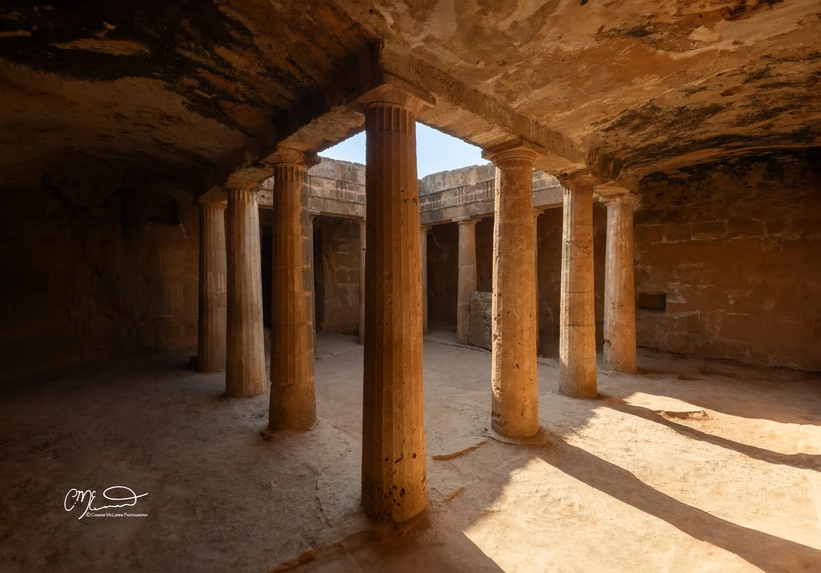 Tomb of the Kings, Cyprus. Ancient ruins with stone columns inside a stone-caved structure, sunlight casting shadows on the ground.