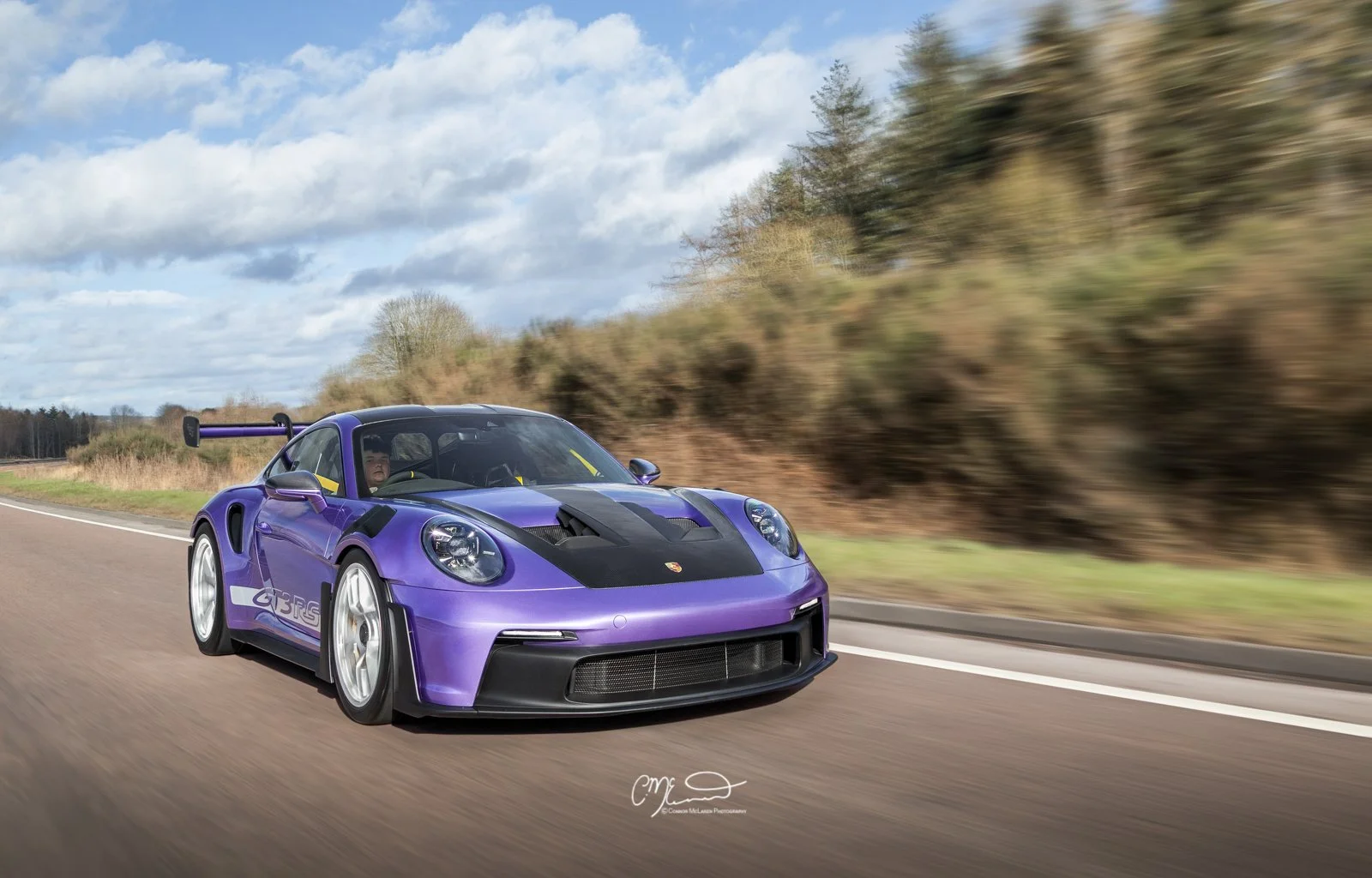 Porsche 911 GT3 RS in Paint to sample purple, weissach.  A purple Porsche 911 GT3 RS racing car driving on a highway with motion blur background and a cloudy sky.
