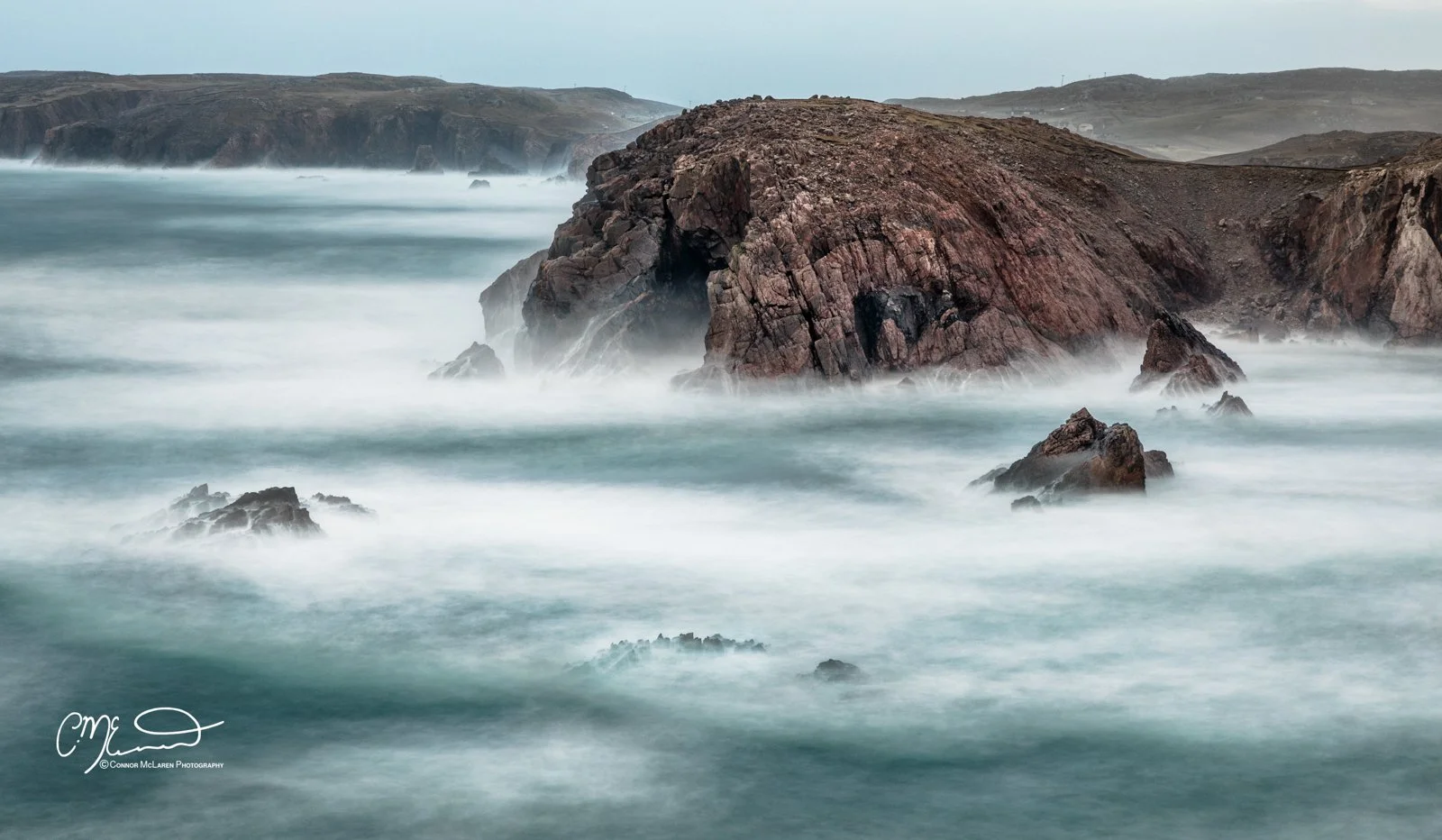 Scotland, Lewis Harris & Outer Hebrides, Mangersta. Rock formations along the coastline with waves crashing around them, foggy and overcast sky in the background.