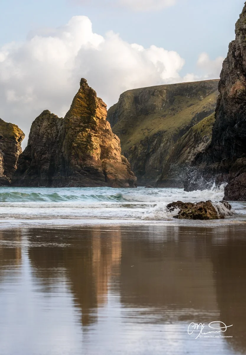 Scotland, Lewis Harris & Outer Hebrides, Tolsta. Rock formations on a beach with waves crashing against the rocks and cloudy sky above.