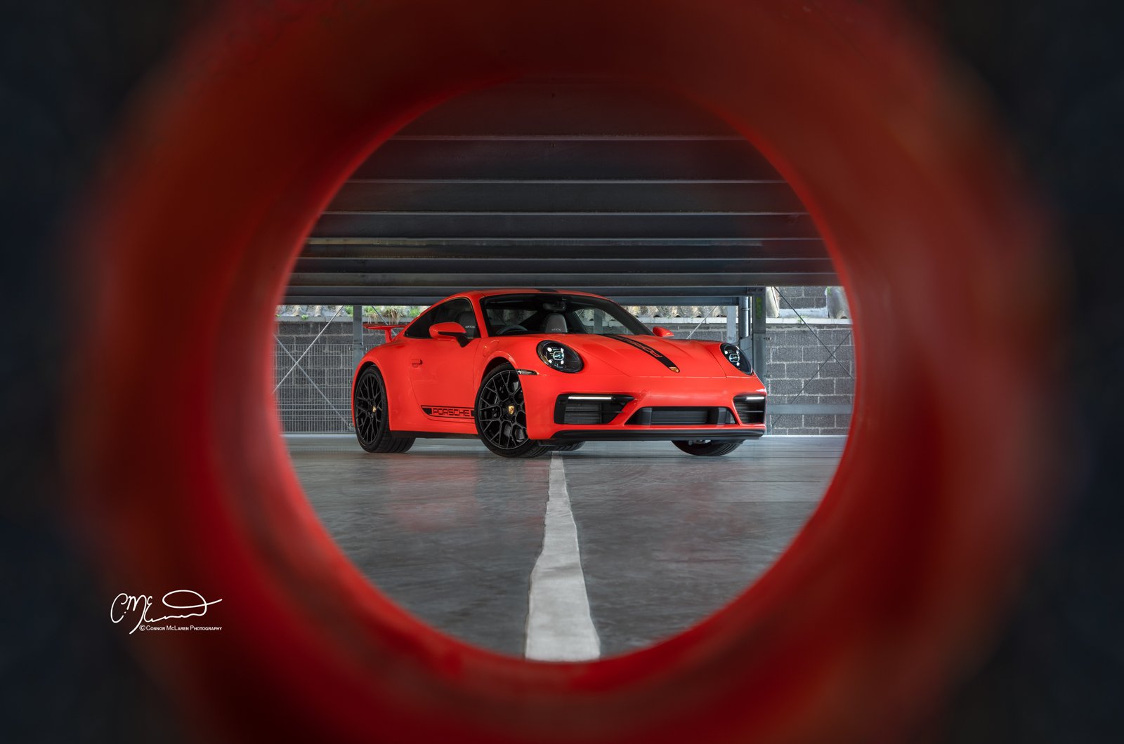 Lava Orange Porsche 911 GTS sports car viewed through a circular opening, parked in an indoor garage.