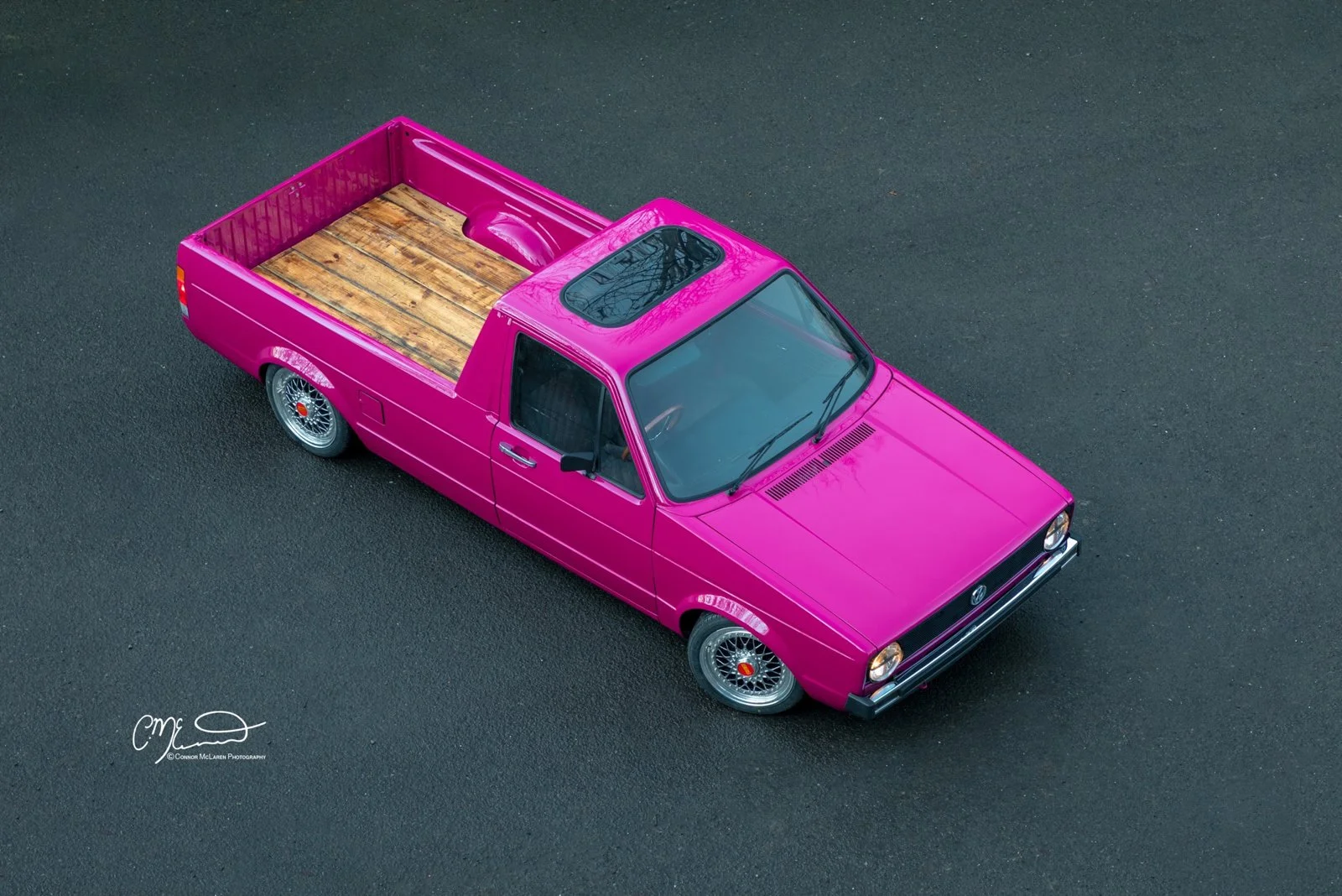 vintage Volkswagen Caddy pickup truck A pink pickup truck with a wooden bed parked on a dark asphalt surface.