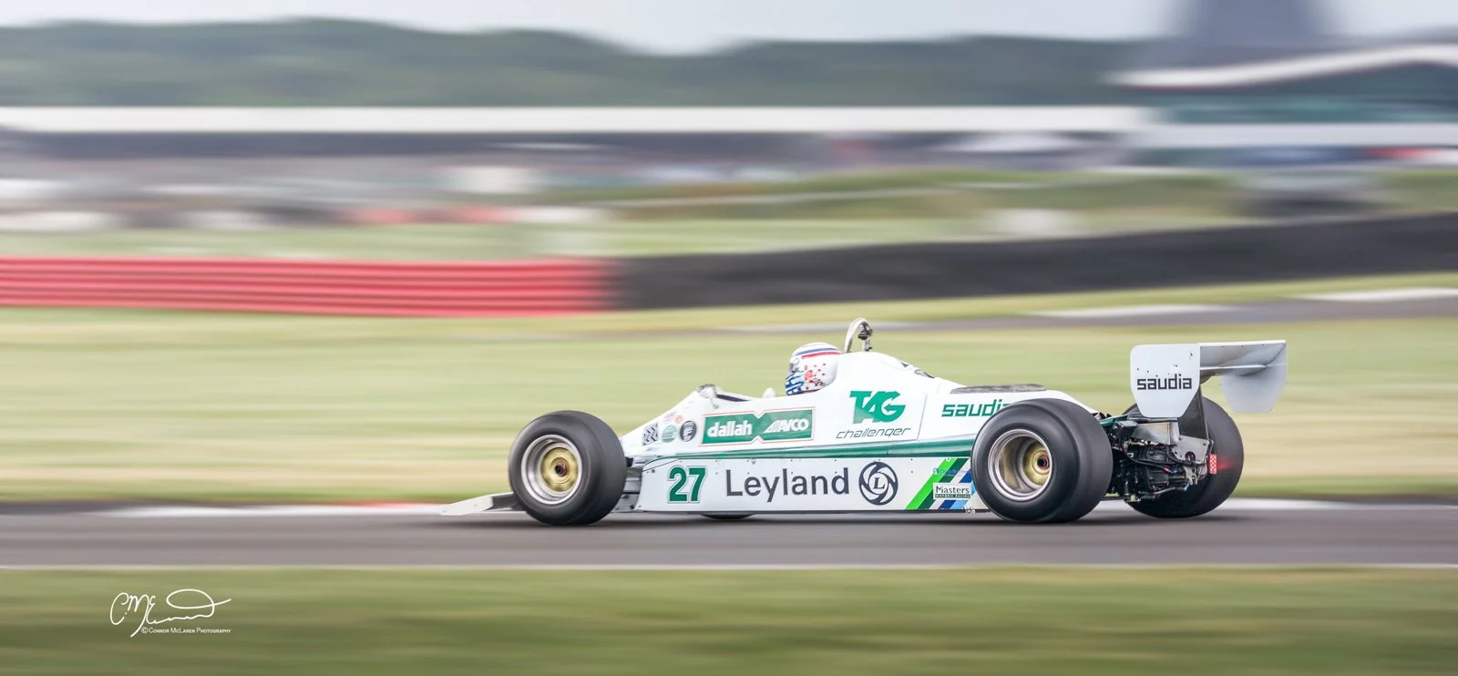 classic Formula one car racing at silverstone. A vintage white Formula 1 race car with the number 27 on its side speeds along a race track, with a blurred background indicating high speed.