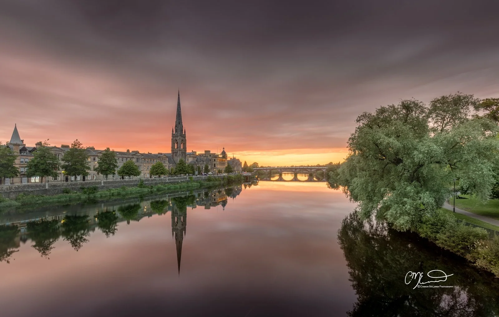 Perth Scotland, Scottish central highlands. Sunset over a river with reflections of a city skyline, church steeple, and trees on the water.