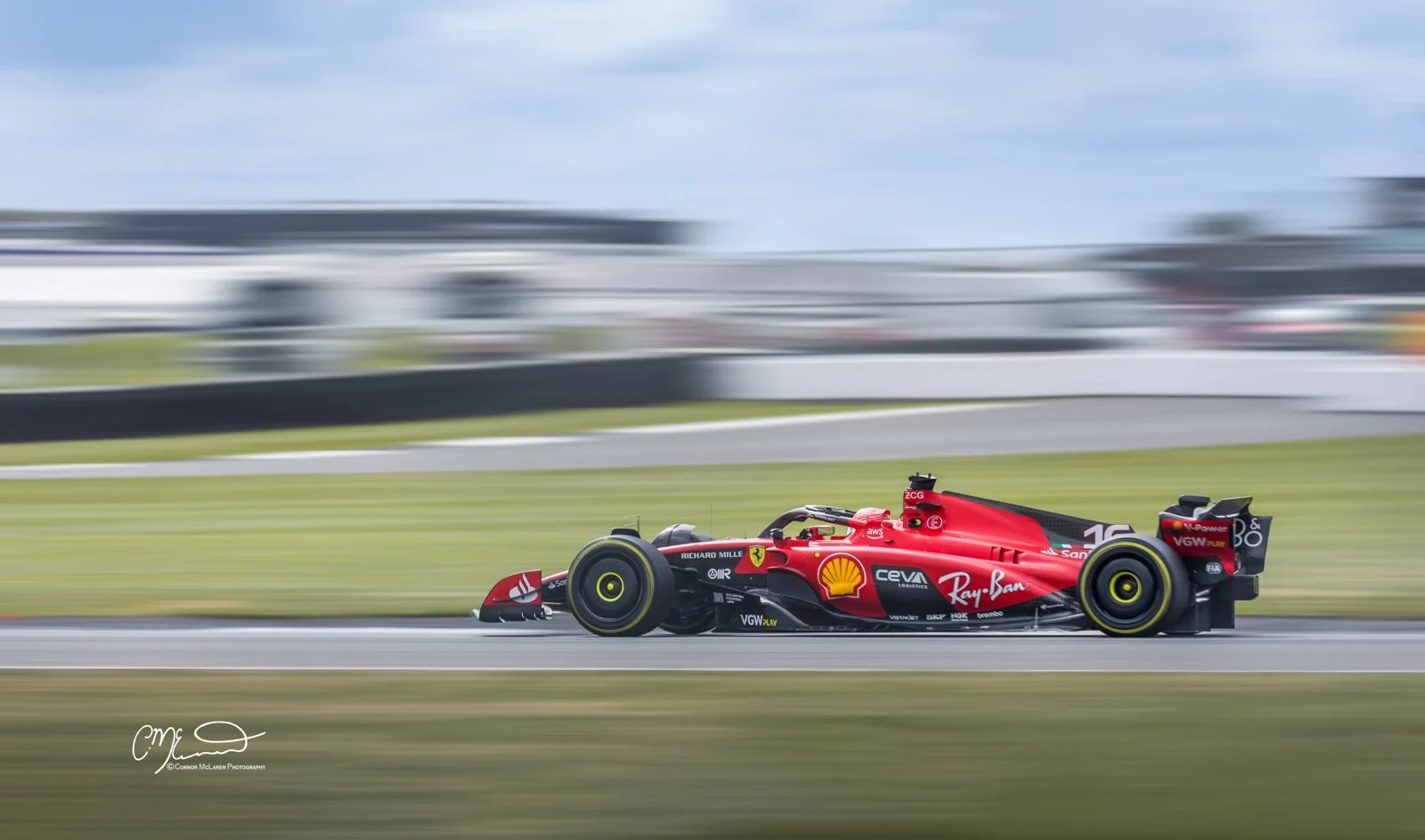 A Ferrari Formula 1 race car speeding on a racetrack with motion blur in the background, featuring sponsorship logos including Shell and Ray-Ban.