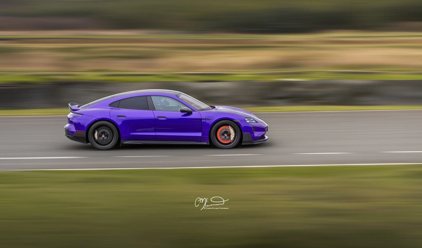 Porsche Taycan Turbo GT in purple racing at Knockhill. Glowing brakes coming into the corner. A purple sports car driving on a highway, with motion blur in the background.