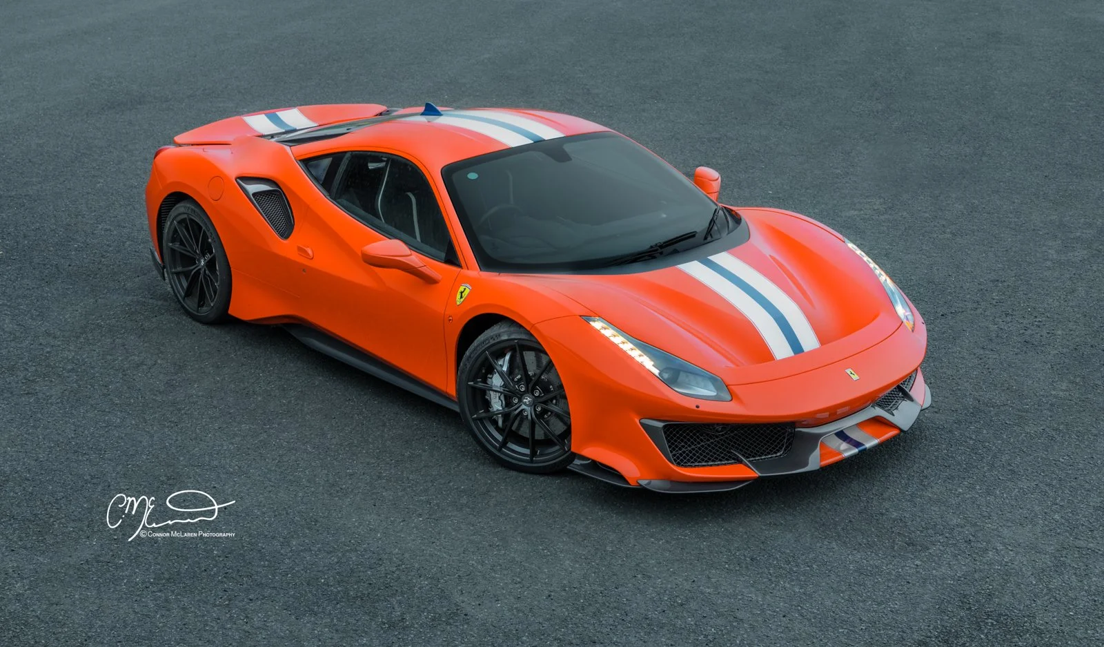 Ferrari 488 Pista. Orange Ferrari sports car with white and blue racing stripes on a dark asphalt surface.