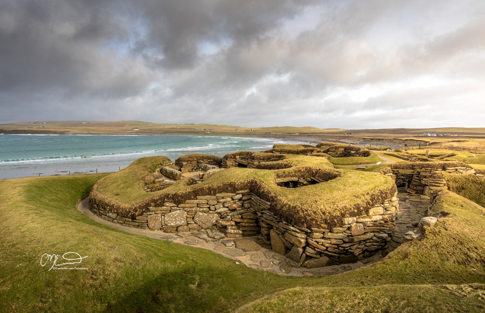 Skara Brae, Orkney, Scotland. Ancient stone ruins on grassy landscape near the sea under a cloudy sky