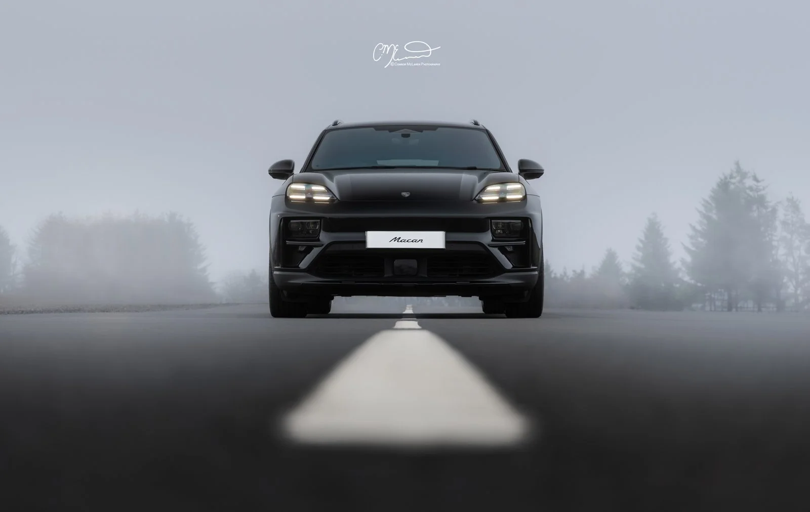 Porsche Macan EV Electric. Front view of a black luxury SUV on an empty road with foggy background and trees.