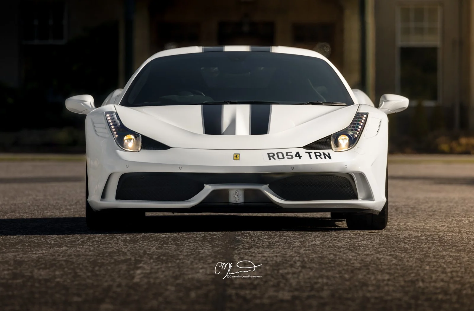 Ferrari 458 Speciale in white at Gleneagles Hotel. Front view of a white Ferrari sports car with black racing stripes, parked on a road.