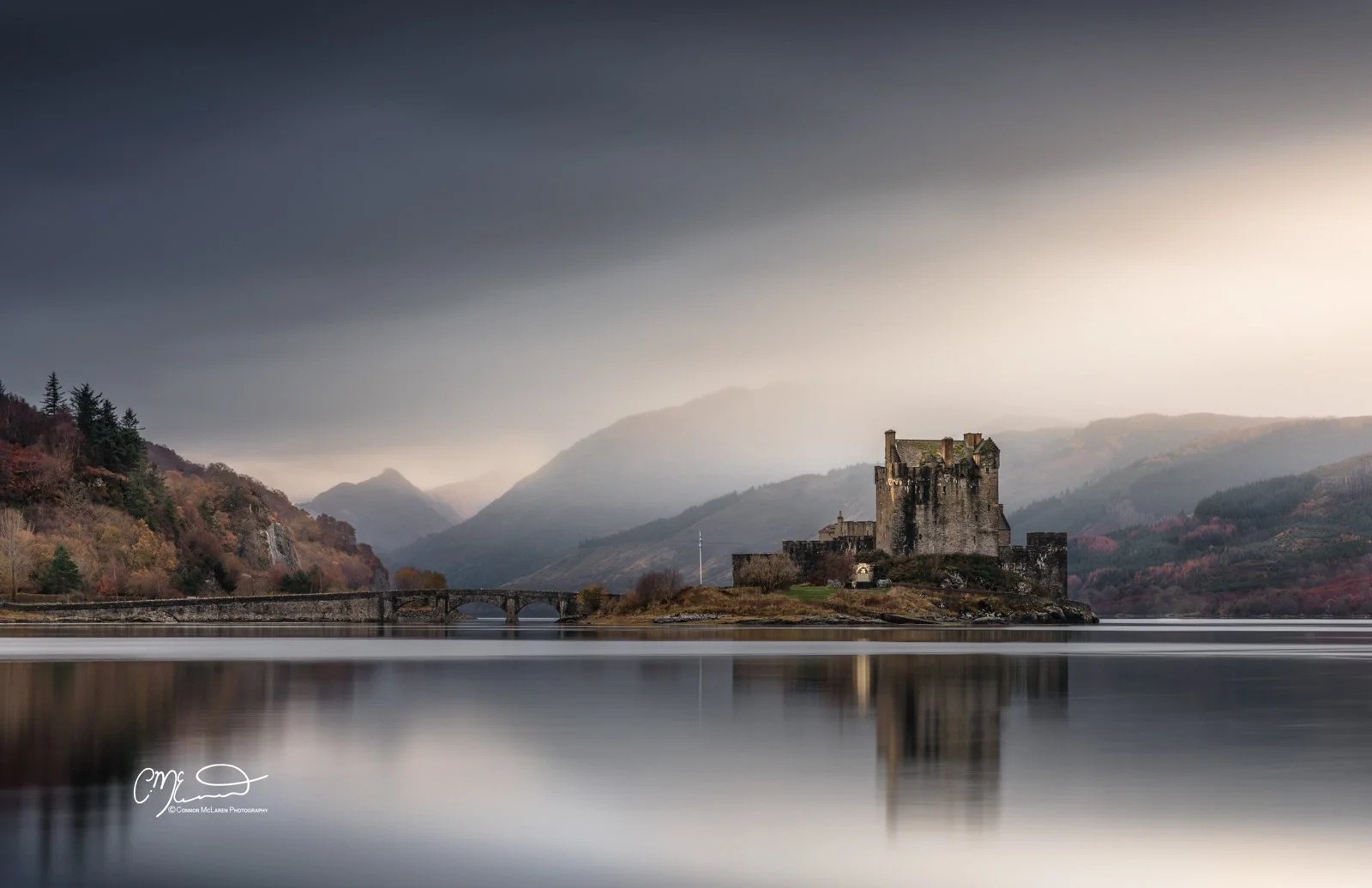 Eilean Donan Castle, Western Highlands, Scotland. A medieval castle on a small island in a lake, with mountains and a cloudy sky in the background.