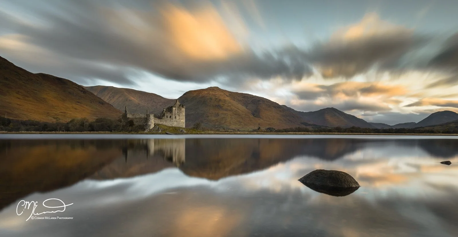 Bucket list locations, Scotland, Loch Awe, Kilchurn Castle. An old castle beside a calm lake with mountains in the background, reflective water, cloudy sky at sunset.