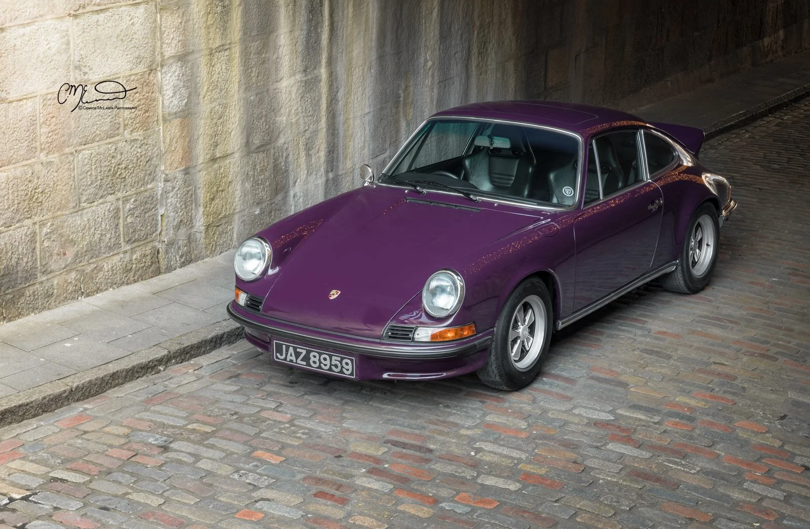 Porsche 911, 2.7RS. A purple vintage Porsche 911 parked on a cobblestone street next to a stone wall.