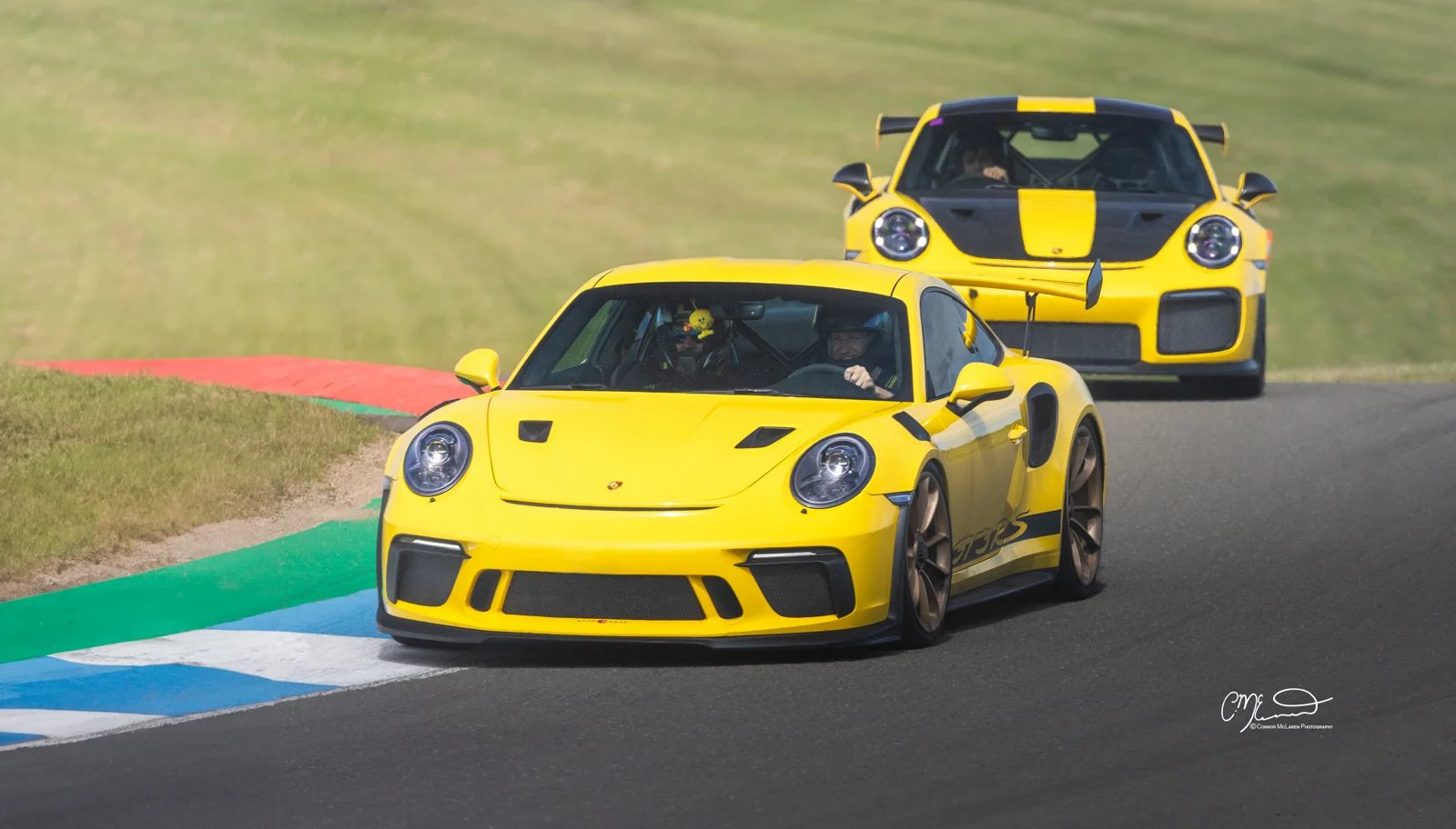 Racing Yellow Porsche GT2 RS, 991, and porsche 911 GT3 RS at Knockhill.Yellow Porsche sports cars racing on a track, with one in front and another behind, on a curving section of the racetrack with colorful painted curbs.
