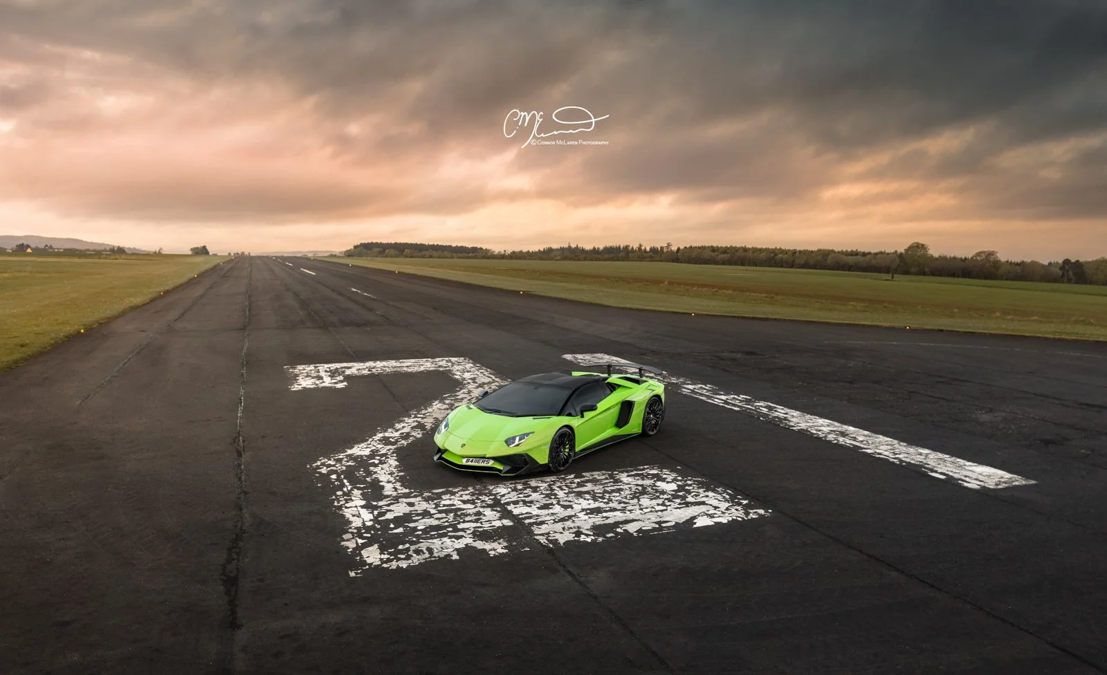 Lamborghini Aventador SV Roaster on airport rA bright green Lamborghini sports car parked on a large airport runway with painted white markings. The runway extends into the distance under a cloudy sky during sunset, with grassy fields o