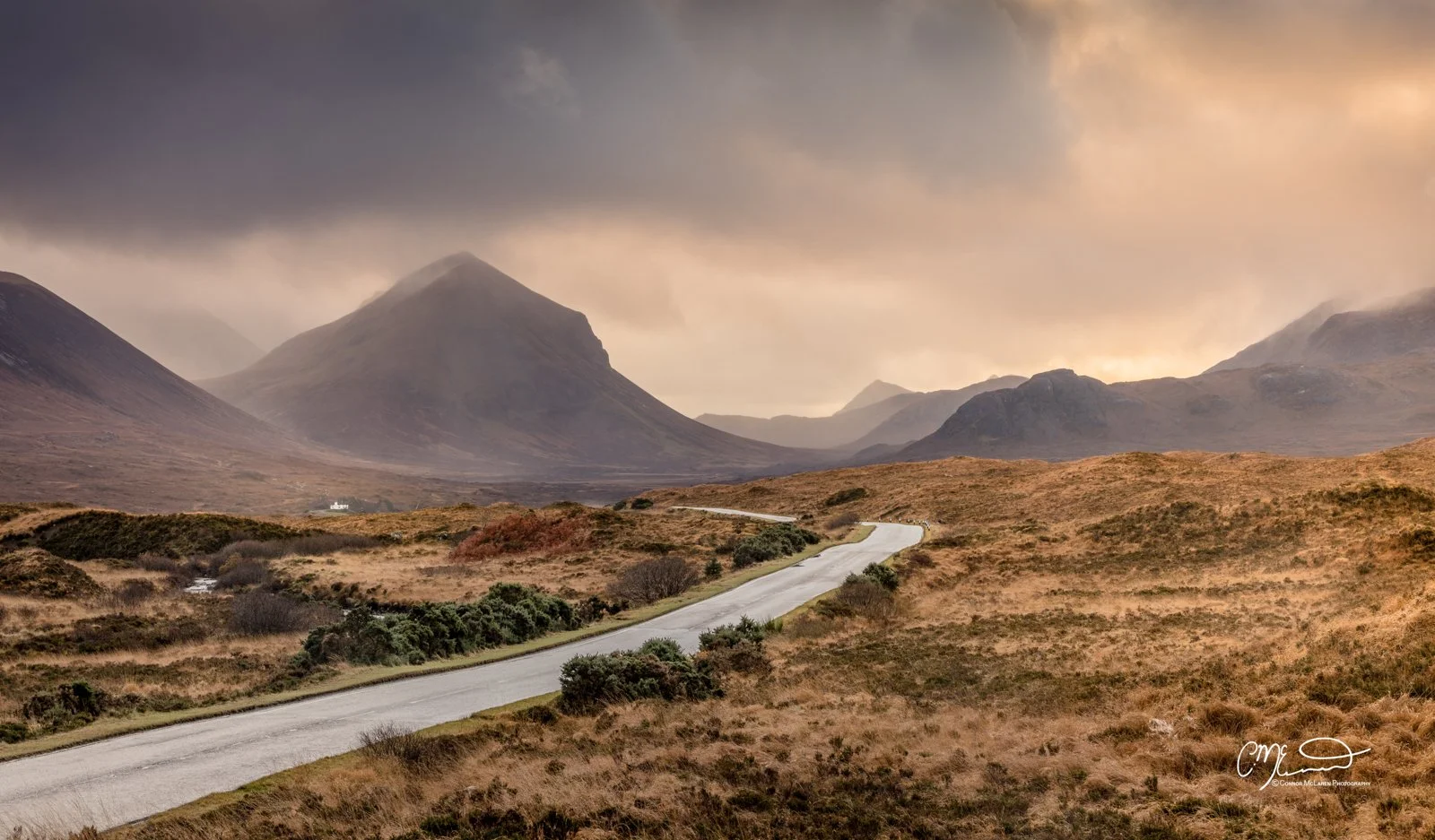 Scotland, Isle of Skye, sligachan. Winding road through a rural landscape with mountains in the background under a cloudy sky during sunset.