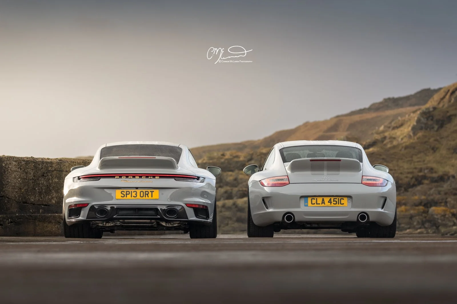 Porsche 911 Sport Classic. A side view of two silver Porsche cars parked outdoors on a road, with hills in the background.