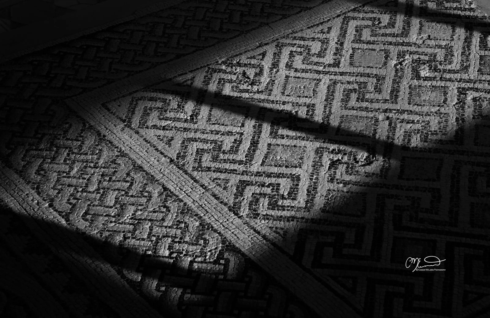 kourion, Cyprus. Close-up of a textured, patterned tile floor with dramatic lighting casting shadows.