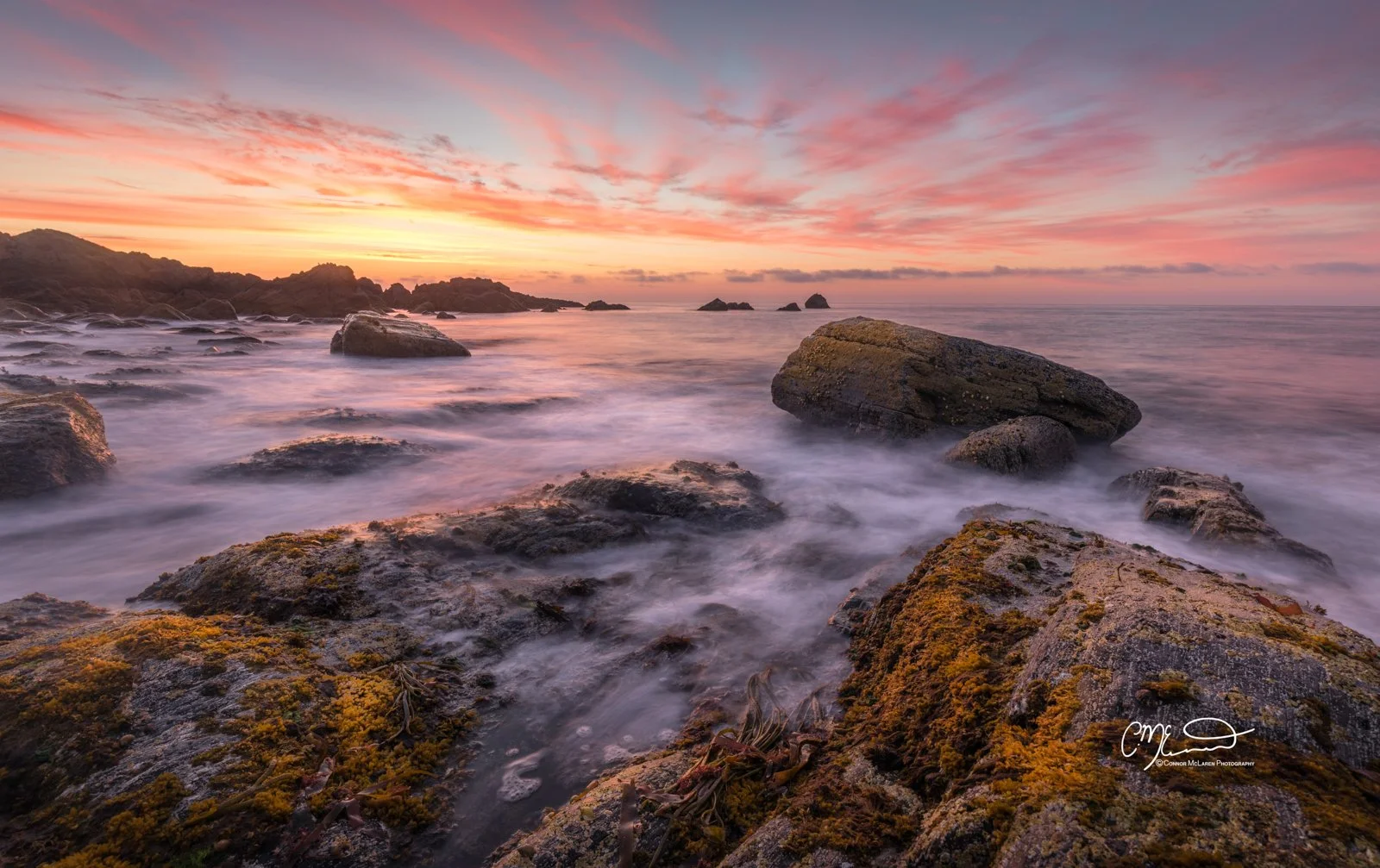 Morrayshire, North East Scotland. Sunset over a rocky shoreline with slow-moving water and pink clouds in the sky.