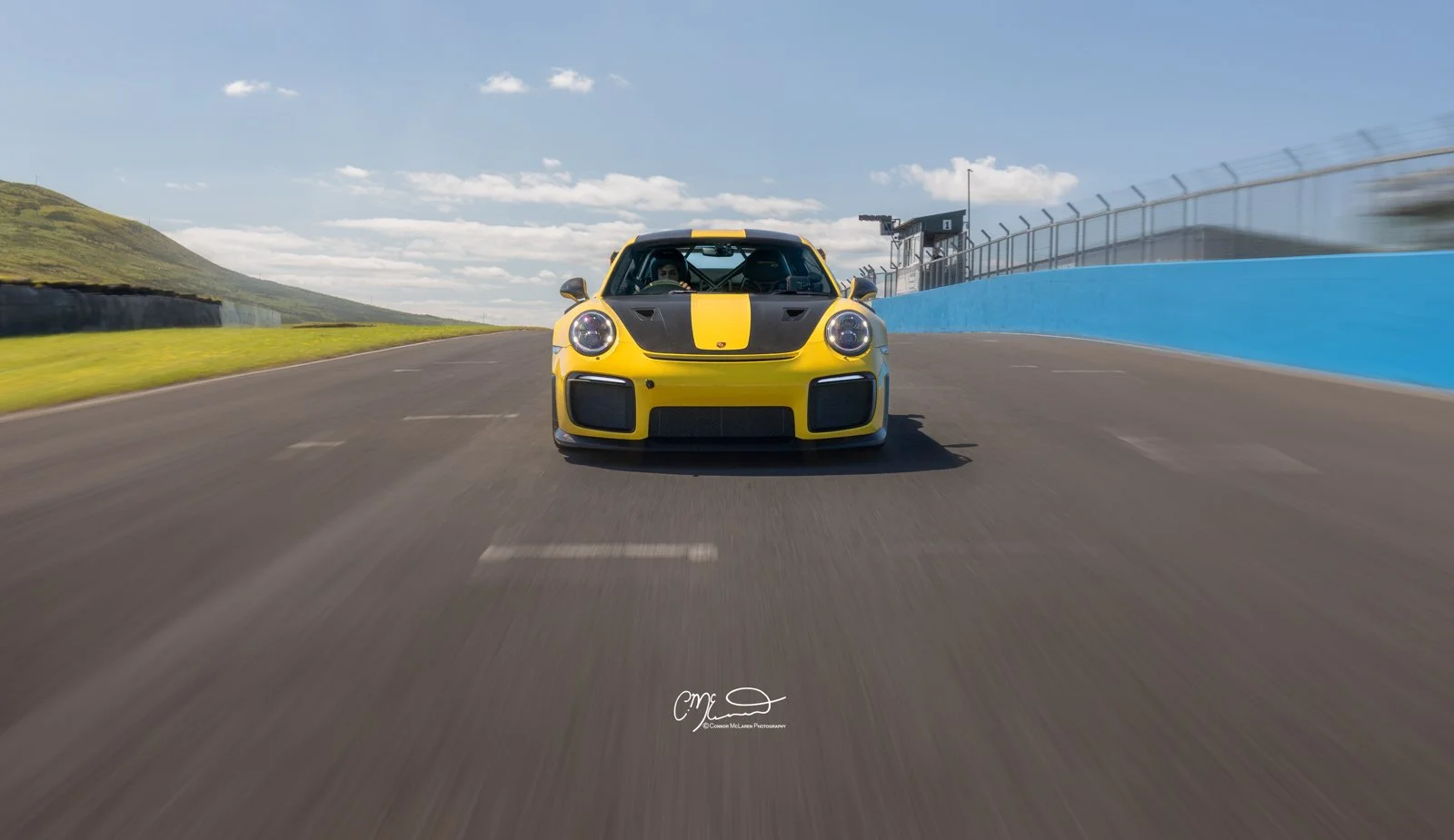 Racing Yellow Porsche GT2 RS, 991, at Knockhill. Yellow race car with black stripes on a racetrack under a partly cloudy sky.